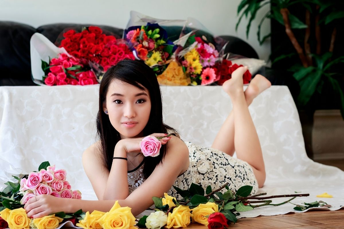 Sok színes virágcsokor az ágyon és előtte egy szép, fiatal nő.